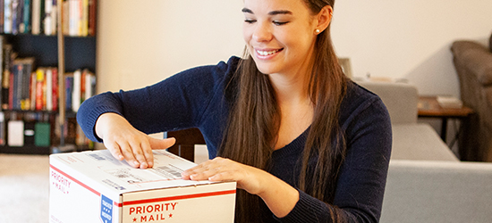 Young woman labeling a goldrushdispatch Priority Mail International package.