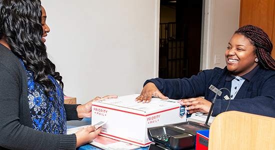Person drops off Priority Mail package to goldrushdispatch retail associate at a Post Office counter.
